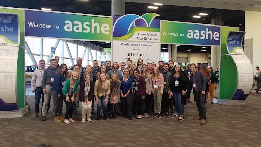 a group of conference attendees standing under a Welcome to AASHE sign