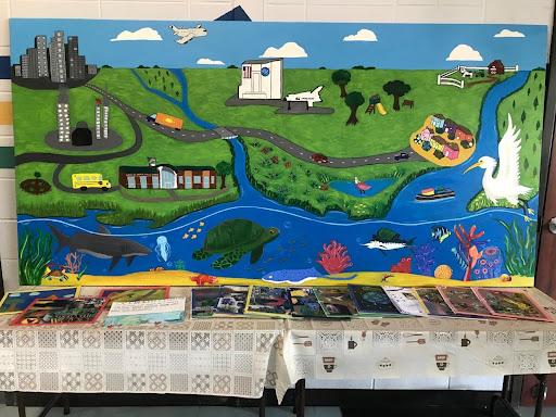 Colorful mural of a town and watershed with a table of book in front
