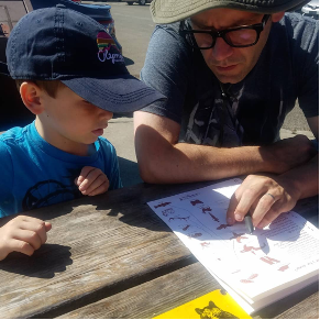 Young child and adult sit at a wooden picnic table looking at pictures of insects