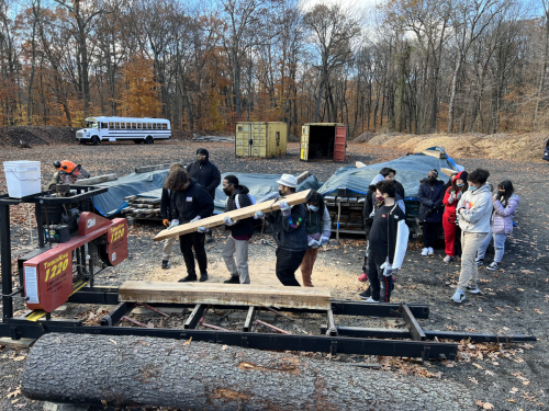 Group of Hartfod High School students participating in Urban Forestry Workshop, feeding large piece of raw lumber through lumber mill.