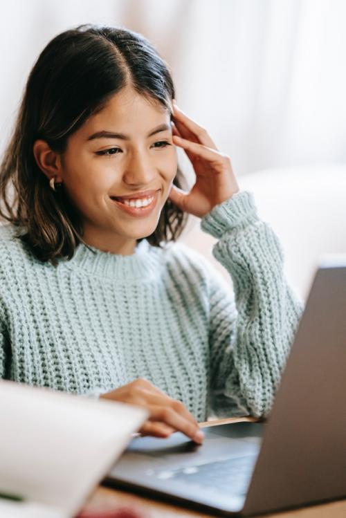 A smiling woman of color looking at a laptop