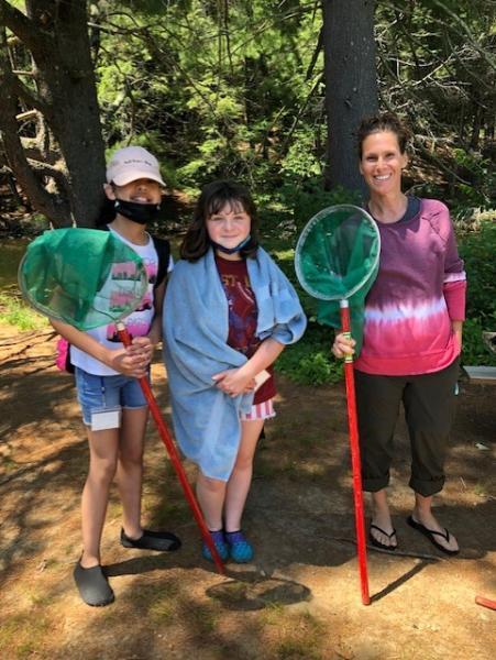 Students and teachers stand in a wooded area holding nets