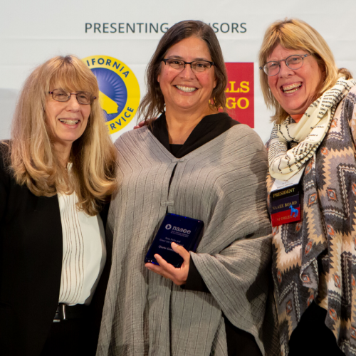 Queta González holding her award in the middle of the photo with Judy Braus and Charlotte Clark on both sides of her