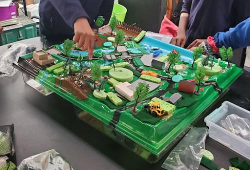 Three students huddle around a model of a wetland and town